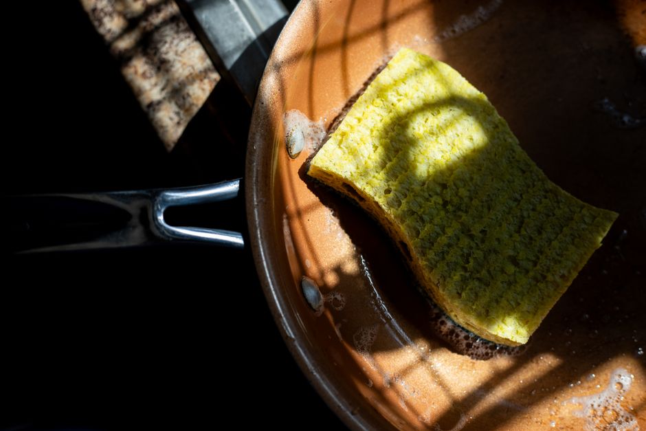 A yellow sponge rests in a copper pan, lit by dramatic shadows. Ideal for cleaning themes.